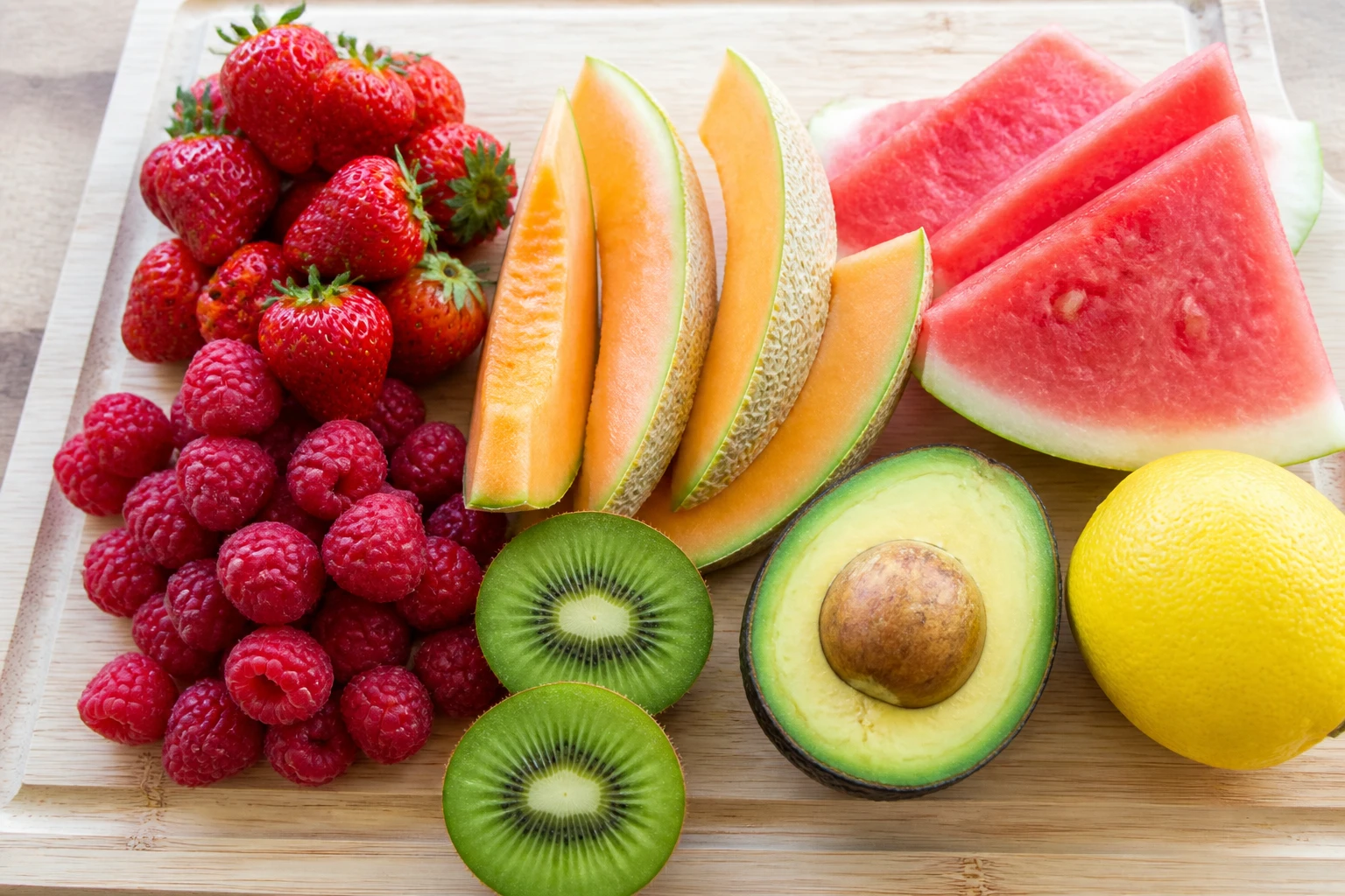 Assortiment de fruits peu sucrés sur planche en bois : fraises, framboises, melon, pastèque, kiwi, citron et avocat