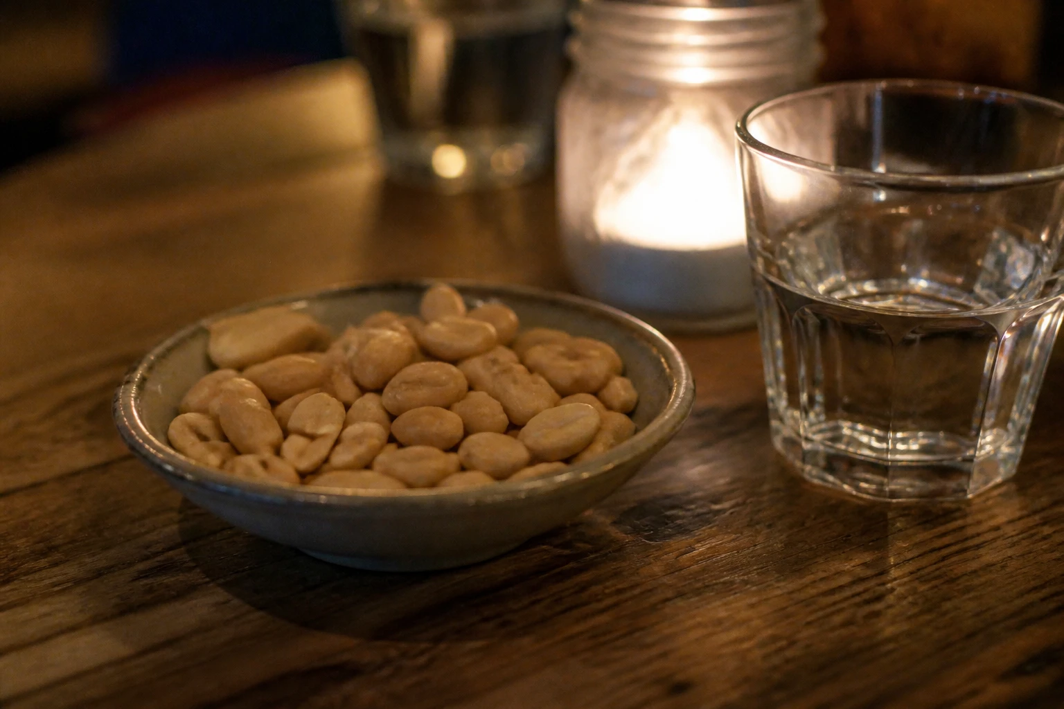 Coupelle de cacahuètes non salées posée sur une table en bois le soir, ambiance tamisée